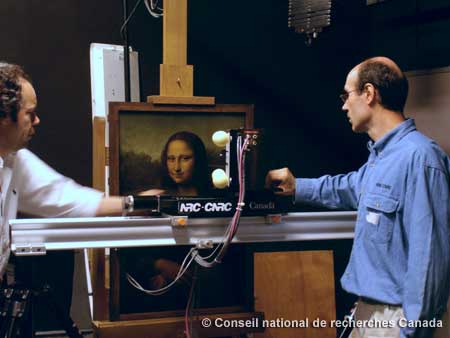 Figure 2 : Luc Cournoyer, du CNRC (à droite) positionne le scanneur devant la peinture pendant qu'un membre du personnel du Centre de recherche et de restauration des musées de France (C2RMF) (à gauche) surveille l'opération.


