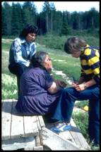 Two nurses talking with an Aboriginal woman outside her home.