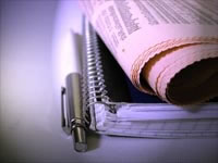 A folded newspaper rests atop a notepad and nearby pen
