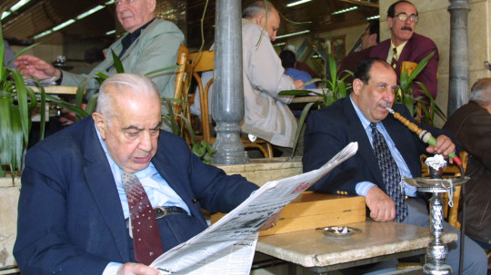 Syrian men read the newspaper and smoke a traditional waterpipe at a cafe in Damascus.