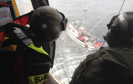 Un Technicien en recherche et sauvetage (à gauche) et un mécanicien de bord de l’ARC observent un bateau depuis la porte utilisée pour les sauvetages d’un hélicoptère CH-149 Cormorant durant l’évacuation sanitaire d’un pêcheur qui avait peut-être un problème de santé, le dimanche 11 août 2013 en soirée.