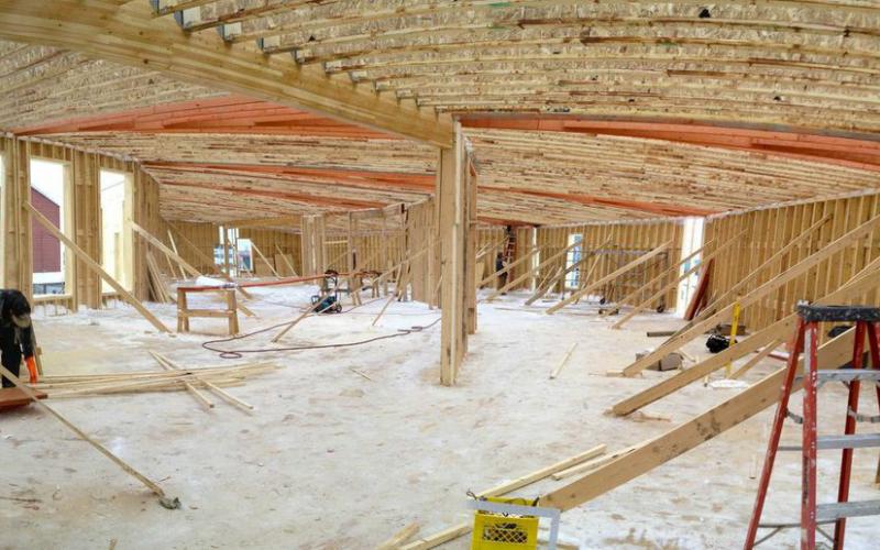 Photo - Two workers, one in foreground and one in background, work on interior trusses of Inuvik’s Children First Centre as construction progresses.