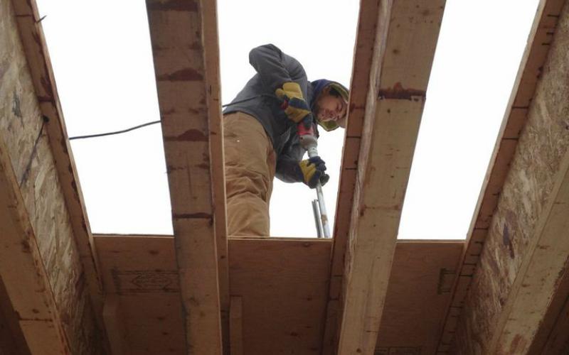 Photo - A worker uses electric equipment to attach roof sheathing during construction of Inuvik’s Children First Centre.