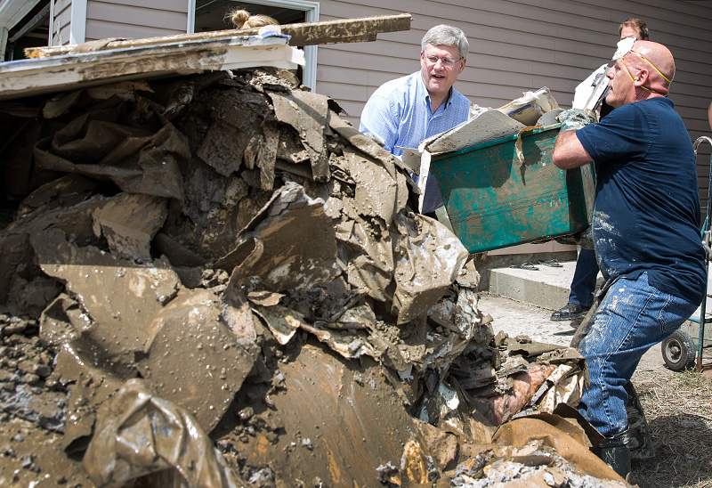 Le Premier ministre Stephen Harper aide  retirer des dbris d'une maison inonde  High River. Le 5 juillet 2013. (Photo par Jill Thompson)