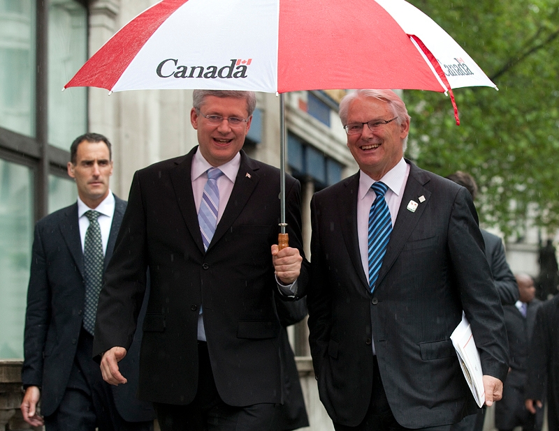 Le Premier ministre Stephen Harper marche sous la pluie en direction de la Maison du Canada, en compagnie de Gordon Campbell, haut-commissaire du Canada au Royaume-Uni,  Londres (R.-U.). 5 juin 2012. (Photo de Deb Ransom)