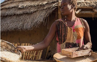 South Sudan: a women prepares sorghum for her family in front of her home.