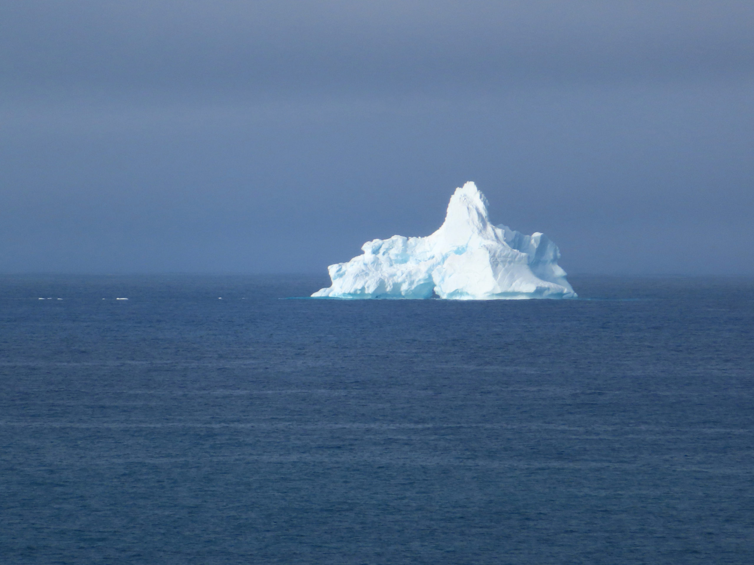 A lone iceberg in dark blue water and distant fog.